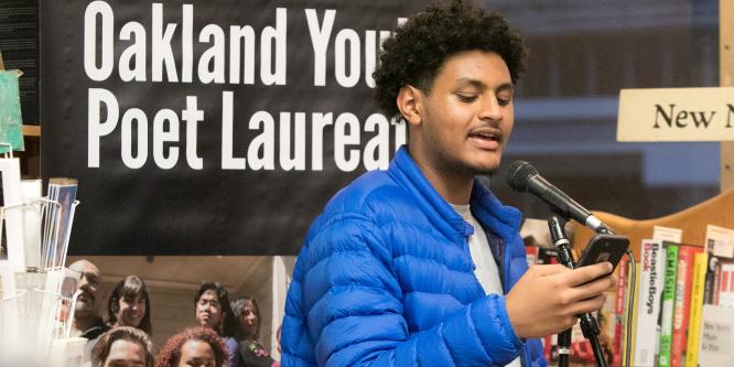 young person is reading a poem from their cellphone into a microphone for a performance in a book store